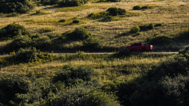 Red Pickup Truck Driving Through Grassy Hills Desktop Wallpaper
