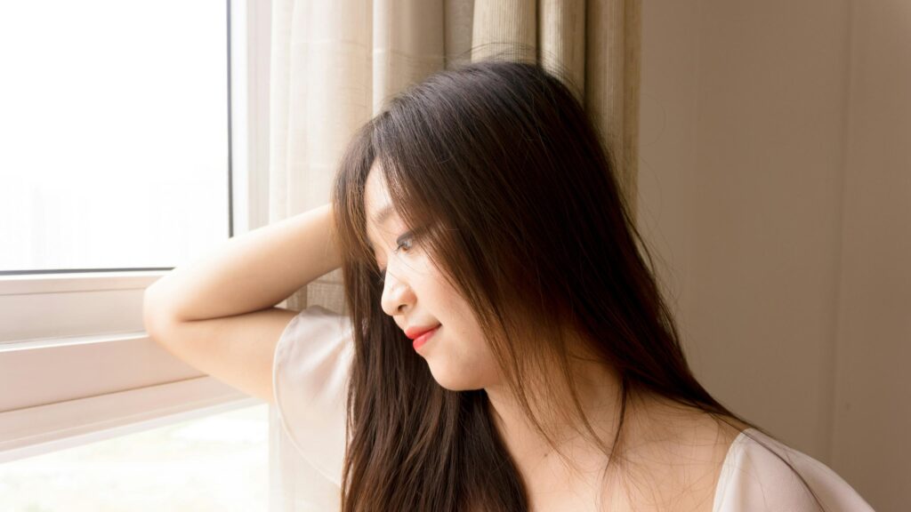 Pensive Asian Woman Looking Through Window 4K Desktop Wallpaper