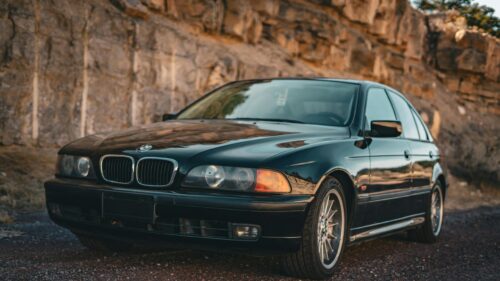 Black BMW E39 Sedan Parked Against Rustic Rock Cliff 4K Wallpaper