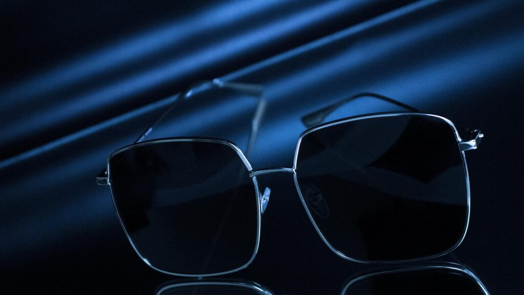 Elegant Minimalist Sunglasses on Reflective Dark Blue Silk Desktop Wallpaper