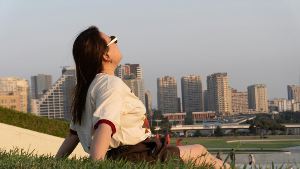 Woman Relaxing on Grassy Hill Overlooking City Skyline 4K Wallpaper