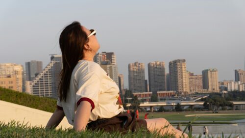Woman Relaxing on Grassy Hill Overlooking City Skyline 4K Wallpaper