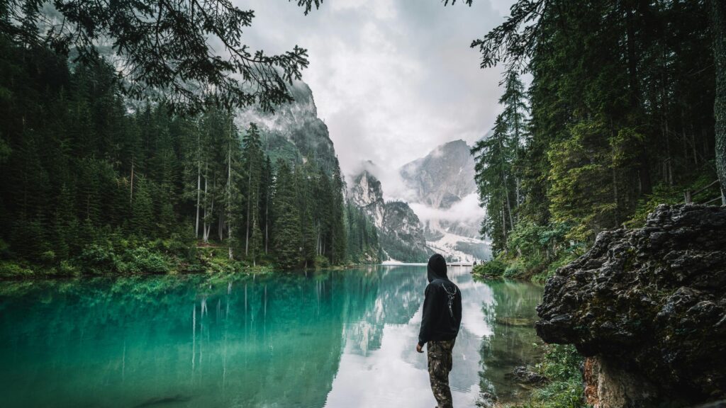 Person Standing by Turquoise Lake in Moody Alpine Mountains Desktop Wallpaper