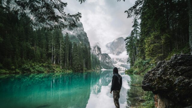 Person Standing by Turquoise Lake in Moody Alpine Mountains Desktop Wallpaper