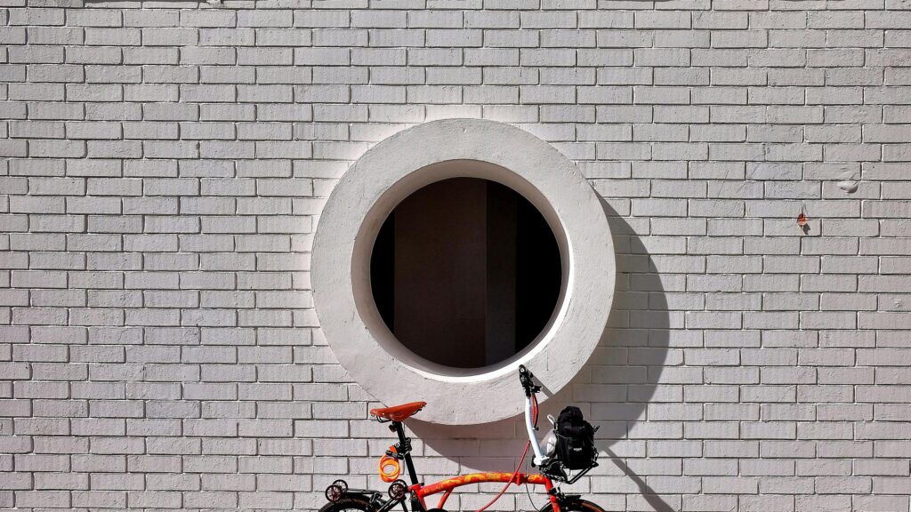 Minimalist Orange Folding Bicycle Against White Brick Wall 4K Wallpaper