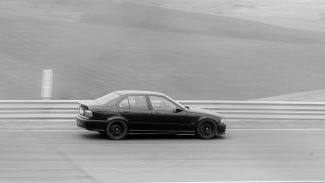 Black BMW E36 Sedan Racing on Track Side Profile 4K Wallpaper