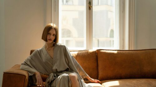 Elegant Woman in Silk Robe Relaxing on Brown Leather Sofa 4K Wallpaper