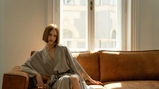 Elegant Woman in Silk Robe Relaxing on Brown Leather Sofa 4K Wallpaper