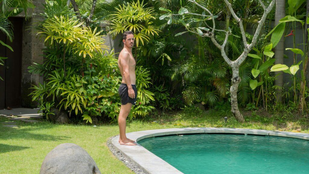 Shirtless Man Standing by Tropical Poolside 4K Wallpaper