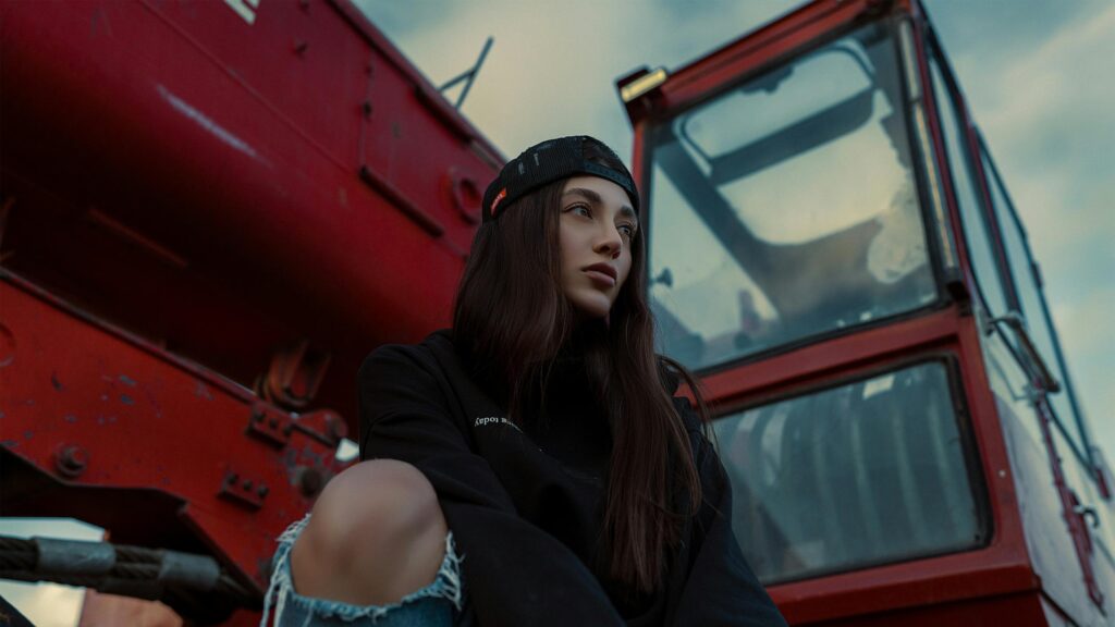Stylish Girl Sitting by Red Industrial Machine Desktop Wallpaper