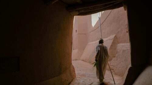 Elder Walking Through Ancient Adobe Passageway Desktop Wallpaper
