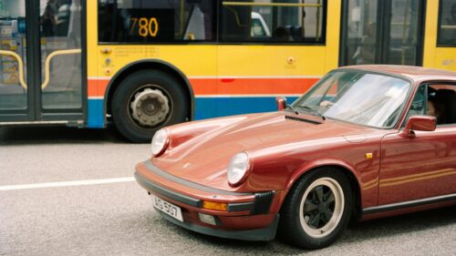 Vintage Maroon Porsche 911 Sportscar Cruising Through City Streets Desktop Wallpaper