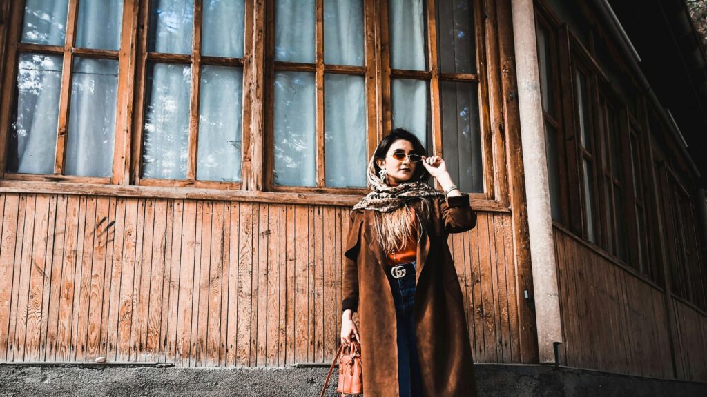 Stylish Woman in Brown Trench Coat Standing by Rustic Wood Wall Desktop Wallpaper