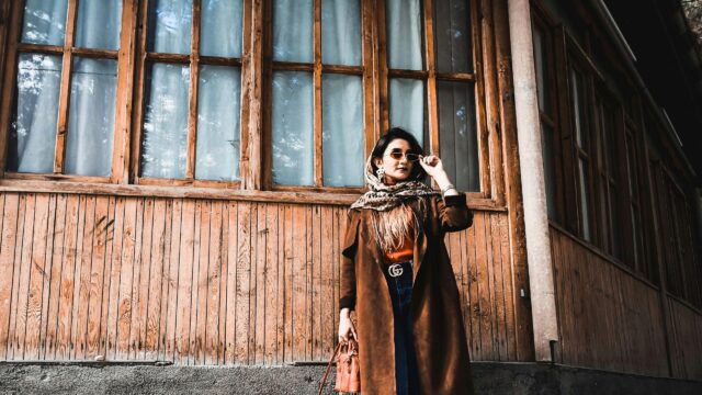 Stylish Woman in Brown Trench Coat Standing by Rustic Wood Wall Desktop Wallpaper