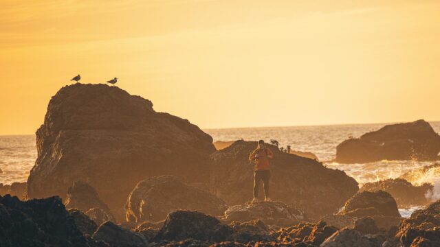 Solo Adventurer Standing on Coastal Rocks at Golden Hour PC Wallpaper