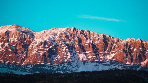 Sun-Kissed Rocky Mountain Peak Under Brilliant Blue Sky 4K Wallpaper