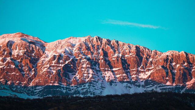Sun-Kissed Rocky Mountain Peak Under Brilliant Blue Sky 4K Wallpaper