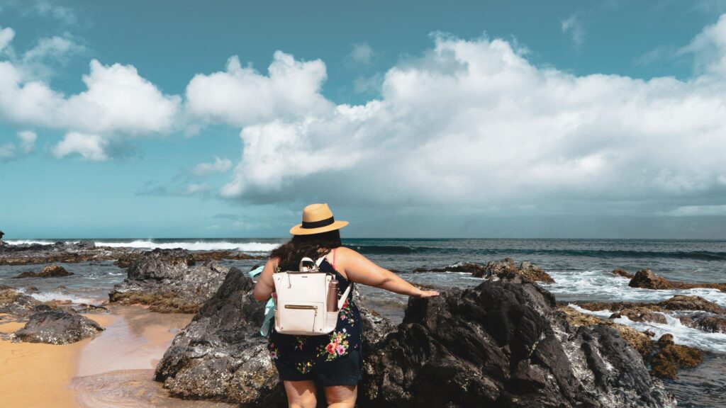Woman Standing on Rocky Tropical Beach with Straw Hat 4K Wallpaper