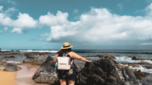 Woman Standing on Rocky Tropical Beach with Straw Hat 4K Wallpaper