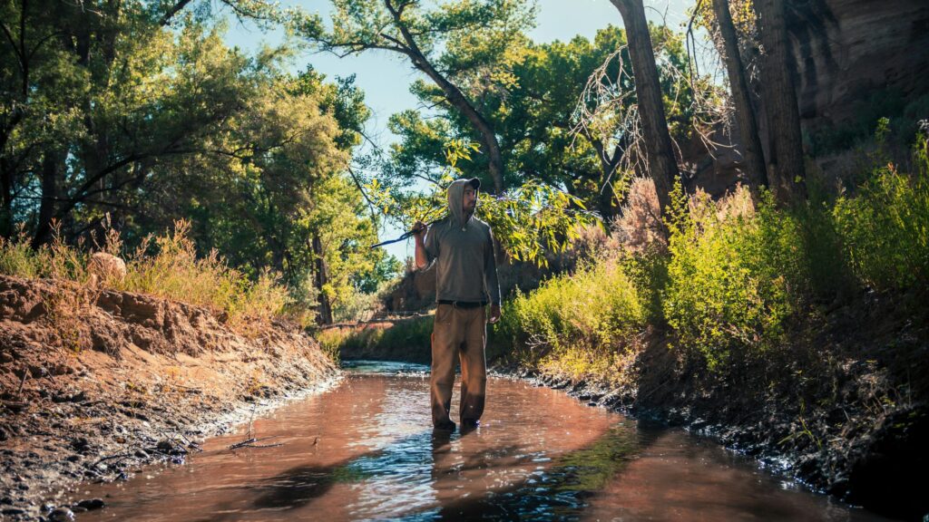 Man Walking in Wilderness River with Tree Branch 4K Desktop Wallpaper