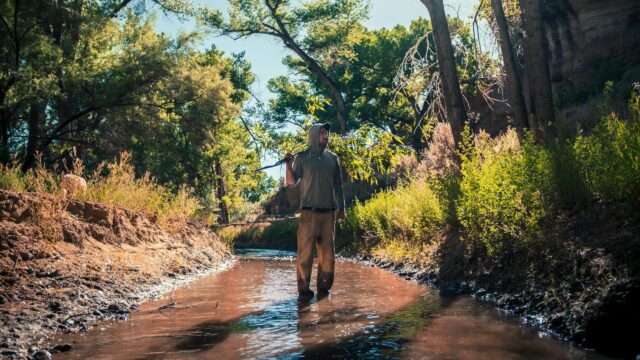 Man Walking in Wilderness River with Tree Branch 4K Desktop Wallpaper