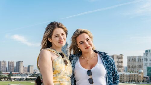 Two Young Women Posing Against a Modern Cityscape PC Wallpaper