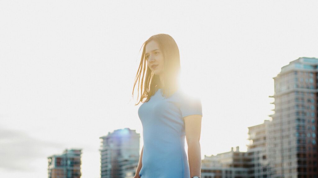 Sun-Kissed Woman in Blue Dress Against Urban Skyline PC Wallpaper