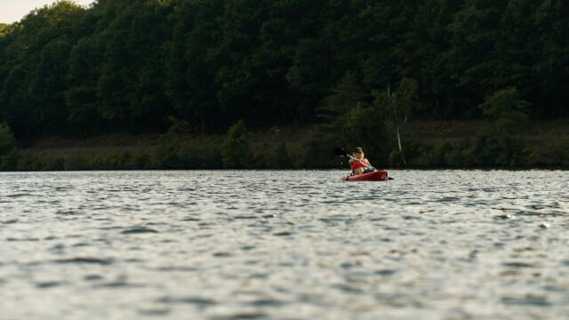Serene Woman Kayaking on Calm Lake at Sunset 4K Desktop Wallpaper