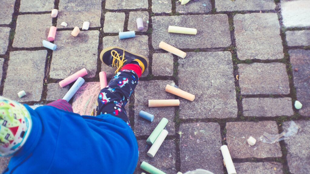Child Playing with Colorful Sidewalk Chalk on Stone Pavement Desktop Wallpaper
