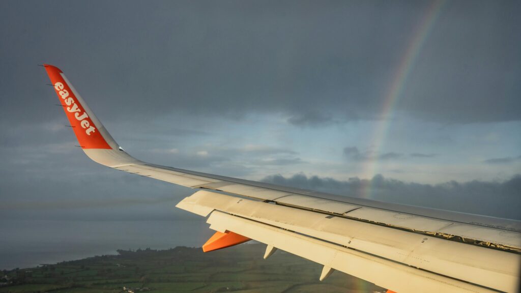 EasyJet Airplane Wing with Rainbow Over Scenic Landscape 4K Wallpaper