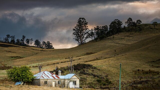 Rustic Stone Cottage in Rolling Hills under Moody Skies Desktop Wallpaper