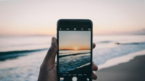 Hand Holding Phone Capturing Sunset Beach View 4K Desktop Wallpaper