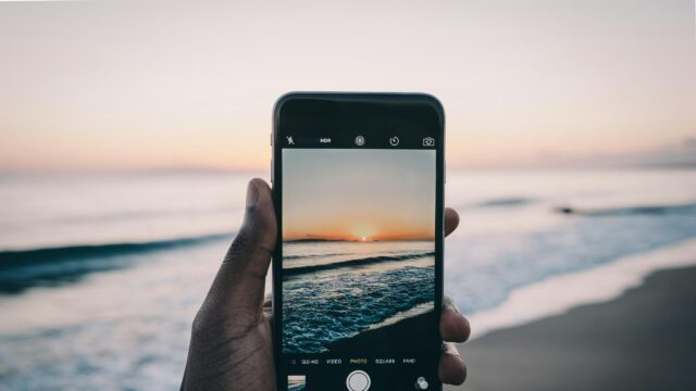 Hand Holding Phone Capturing Sunset Beach View 4K Desktop Wallpaper