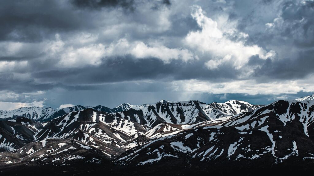 Dramatic Snowy Mountain Range Under Stormy Clouds 4K Wallpaper