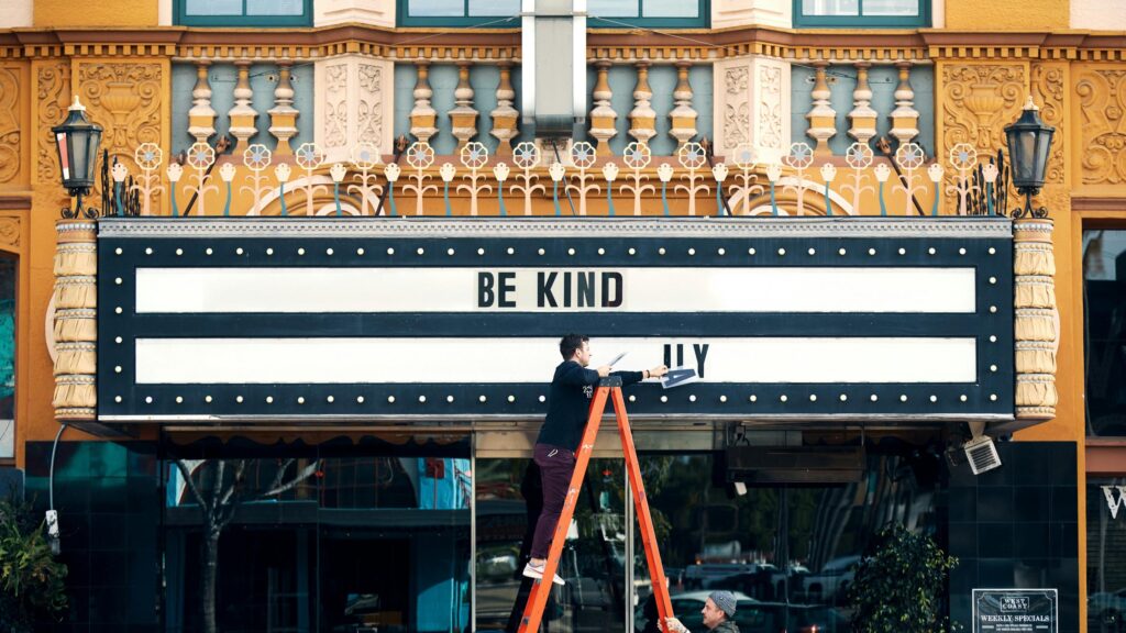 Man Placing Be Kind Lettering on Historic Theater Marquee 4K Wallpaper