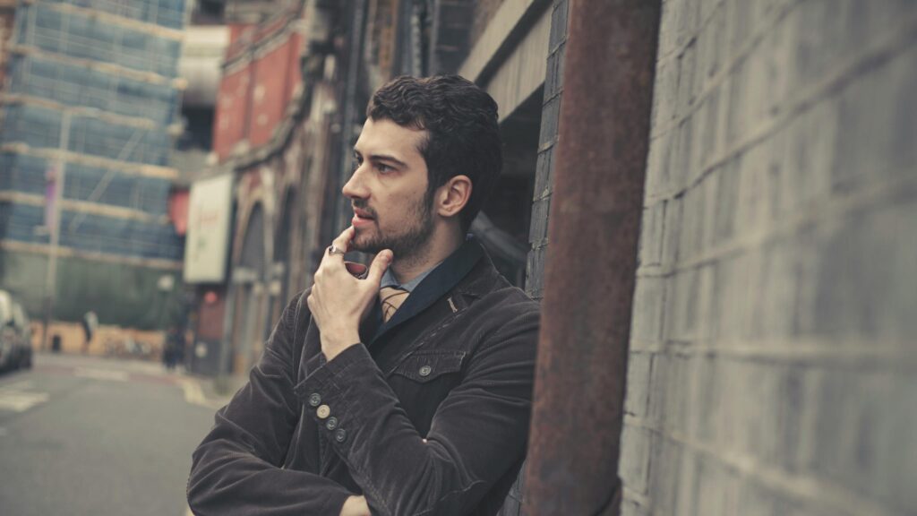 Thoughtful Man in Corduroy Jacket Leaning Against Brick Wall Desktop Wallpaper