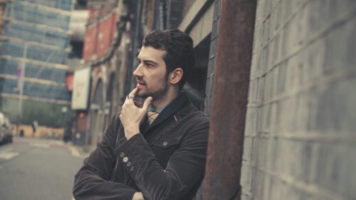 Thoughtful Man in Corduroy Jacket Leaning Against Brick Wall Desktop Wallpaper