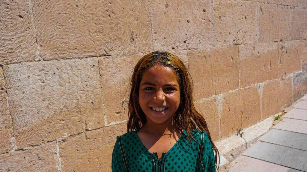 Smiling Girl with Sun-Kissed Hair Against Ancient Stone Wall 4K Wallpaper