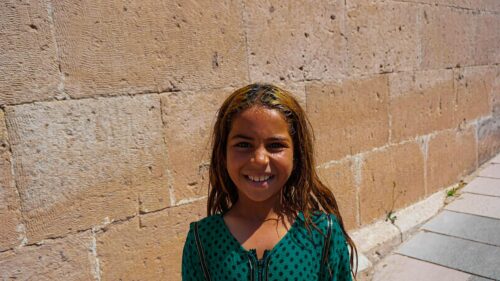 Smiling Girl with Sun-Kissed Hair Against Ancient Stone Wall 4K Wallpaper