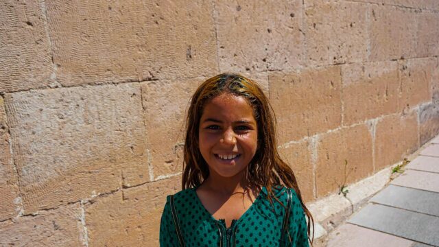 Smiling Girl with Sun-Kissed Hair Against Ancient Stone Wall 4K Wallpaper