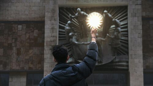 Person Holding a Glowing Sun Symbol in Front of a Statue Desktop Wallpaper