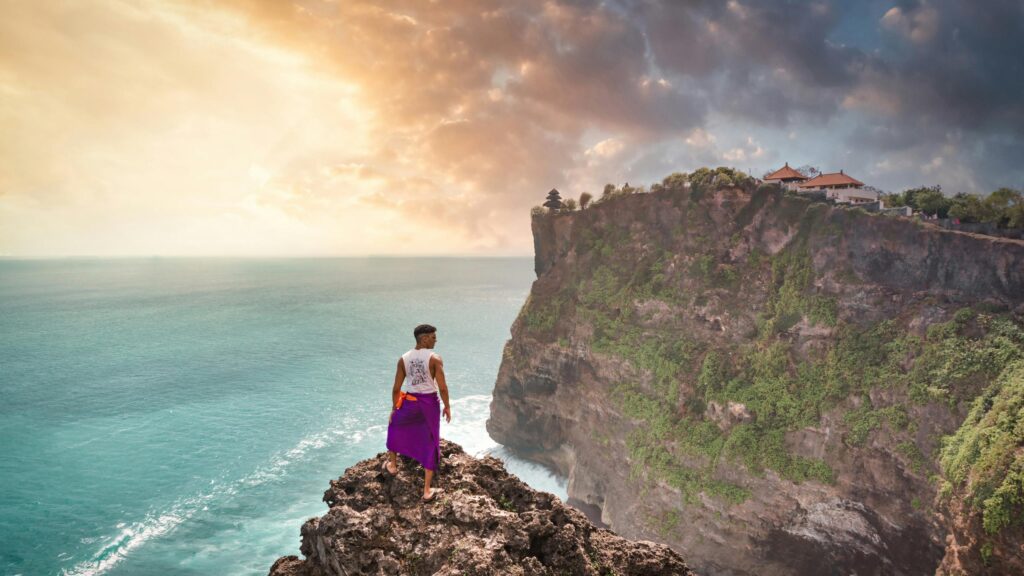 Man Standing on Cliff Overlooking Uluwatu Temple Bali 4K Wallpaper