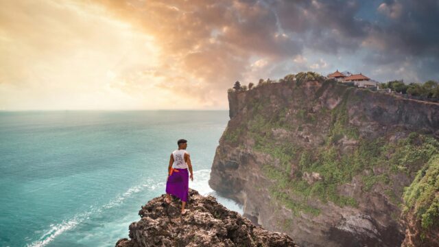 Man Standing on Cliff Overlooking Uluwatu Temple Bali 4K Wallpaper