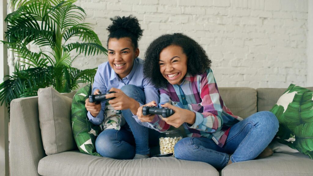 Excited Sisters Playing Video Games on Couch Desktop Wallpaper