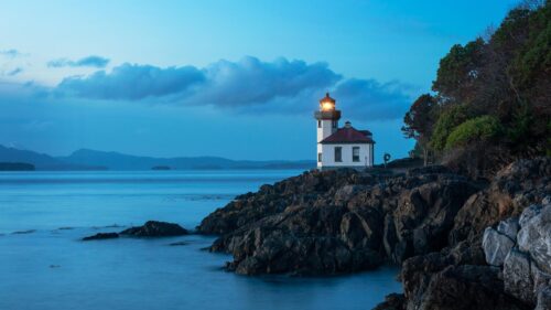 Lit Lighthouse on Rocky Coastline at Twilight 4K Wallpaper