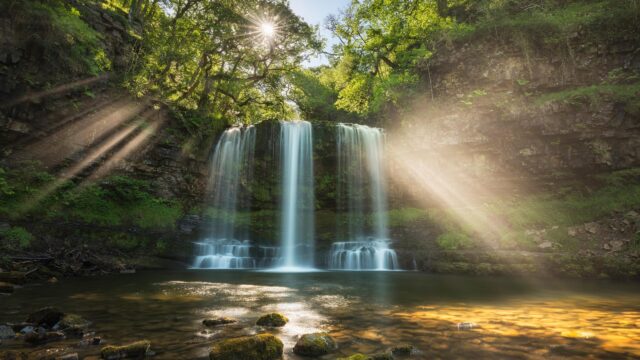 Sunlight Piercing Through Lush Forest Waterfall 4K Desktop Wallpaper